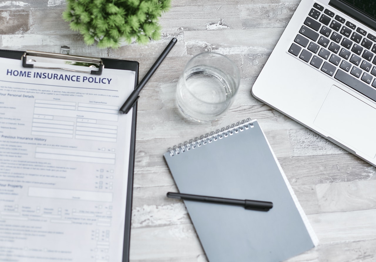 A notebook, home insurance policy, and laptop on the table